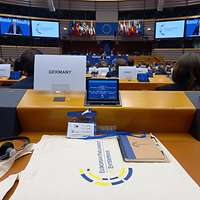 Blick über den Tisch mit Unterlagen und Display in den Hemicycle beim EPdU 2023