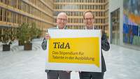 Oliver Heikaus und Jens Brandenburg halten ein Schild zu TidA in die Höhe