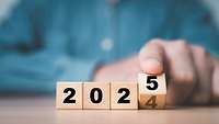 Eine Hand kippt bei vier Würfeln den letzten, sodass 2024 zu 2025 wird