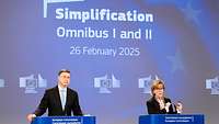 Mann und Frau an einem Podium vor einer Projektion "Simplification Omnibus I and II"