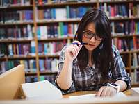 Junge Frau beim Studium von Büchern vor einem Bücherregal