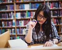 Junge Frau beim Studium von Büchern vor einem Bücherregal