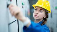 Frau mit blauem Overall und gelbem Bauhelm an einer Magnettafel