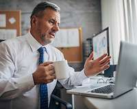 Geschäftsmann am Laptop gestikuliert, eine Tasse in der Hand